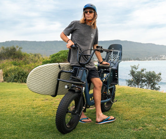 Vamos surfboard rack arms carrying a board alongside the bike