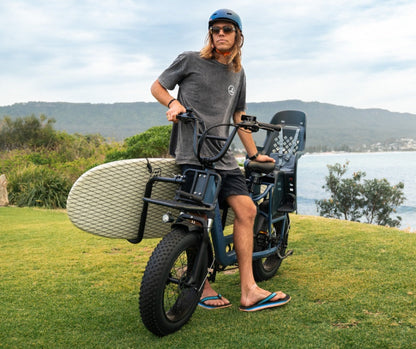 Vamos surfboard rack arms carrying a board alongside the bike